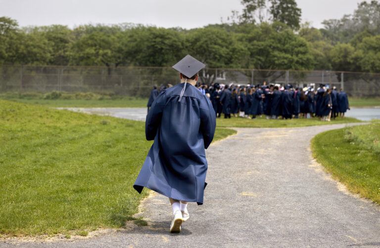A graduate in gown and cap rushes to join a group of classmates.