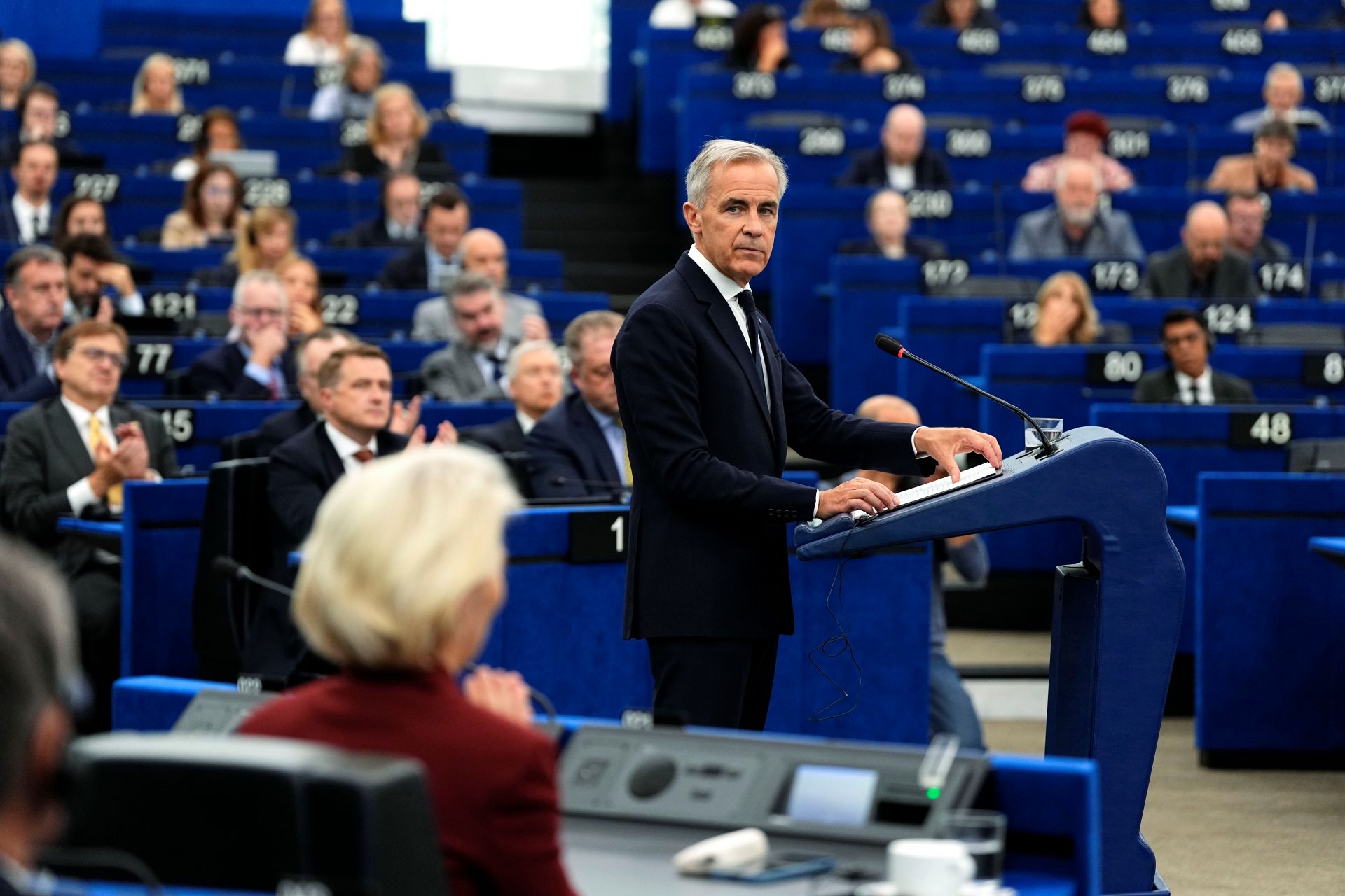Le Premier ministre Mark Carney, debout derrière un pupitre, regarde la présidente de la Commission européenne, Ursula von der Leyen, assise à sa gauche, alors qu’il s’adresse au Parlement européen.