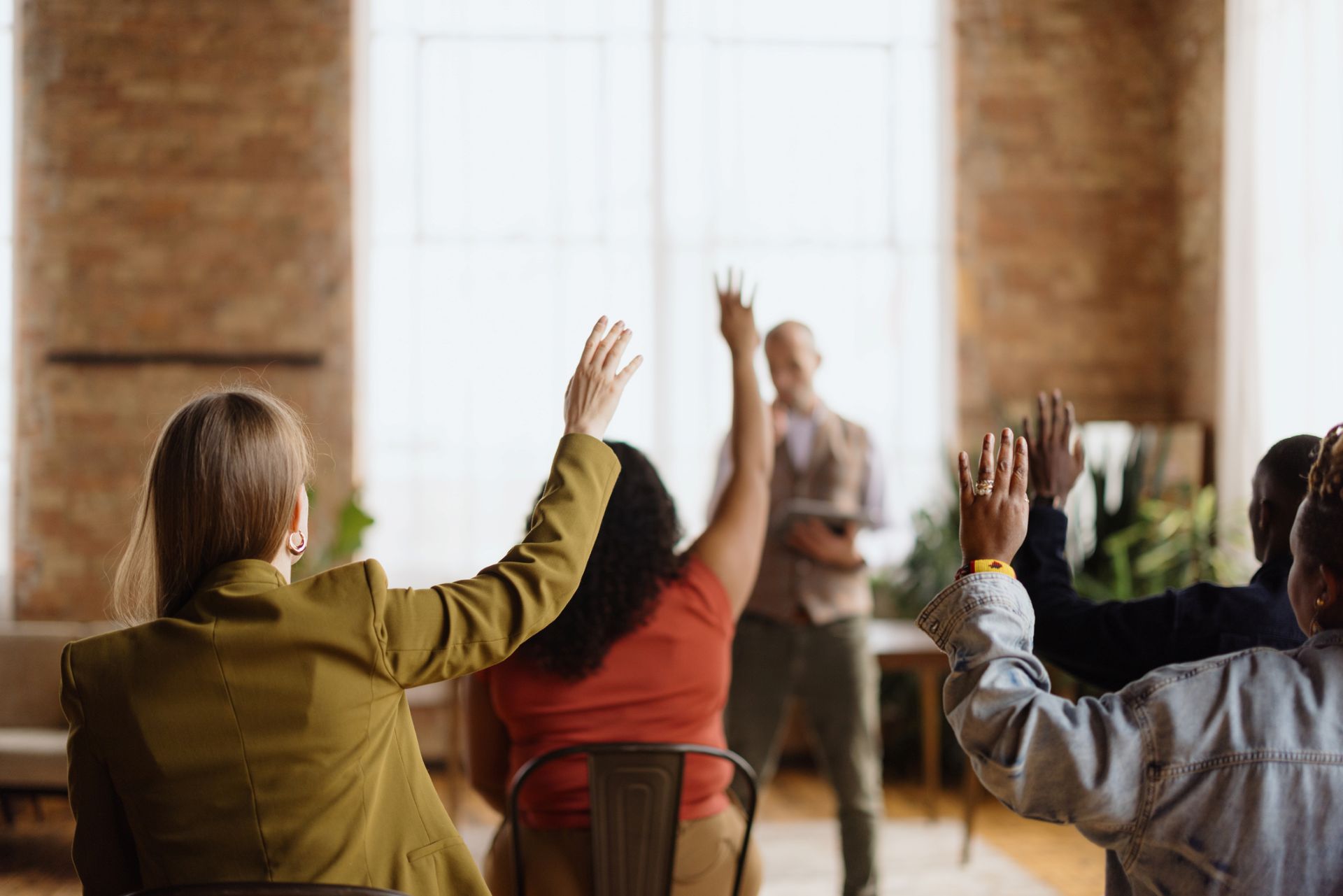 People with their backs to the camera have their hands raised in a stock-photo meeting.