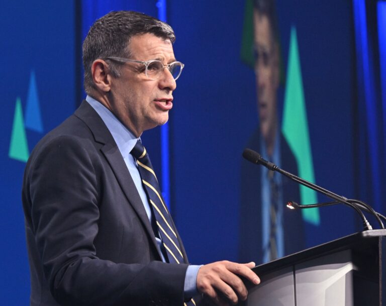 Un homme en habit et cravate s’exprime au pupitre lors d’une allocution, devant un microphone.