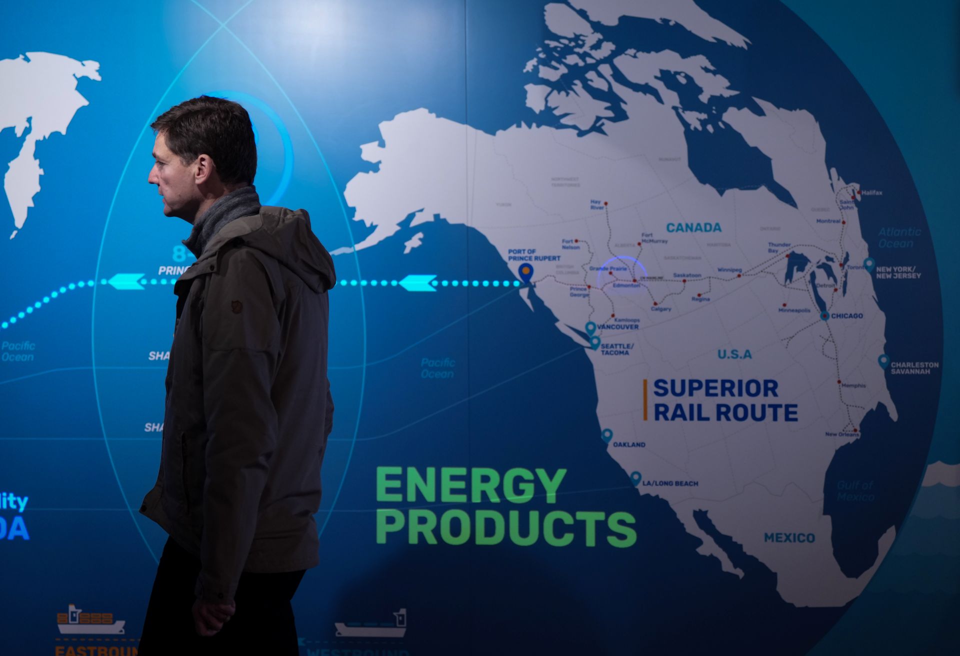 NDP leader David Eby walking away from a map showing trade routes in Canada and a large arrow heading west from B.C.