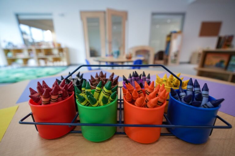 Brightly coloured crayons in pots with an empty daycare centre in the background.