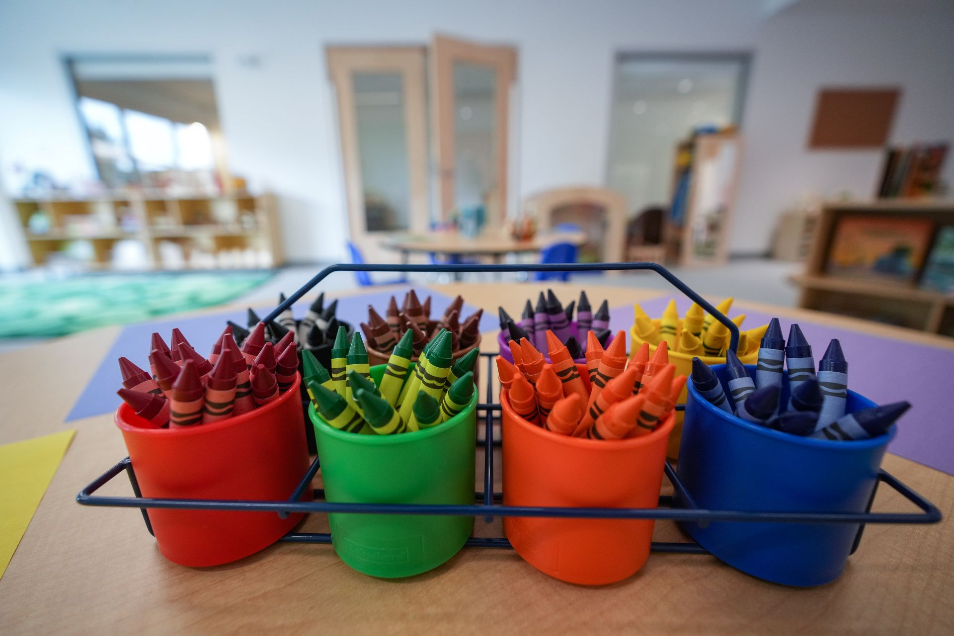Brightly coloured crayons in pots with an empty daycare centre in the background.