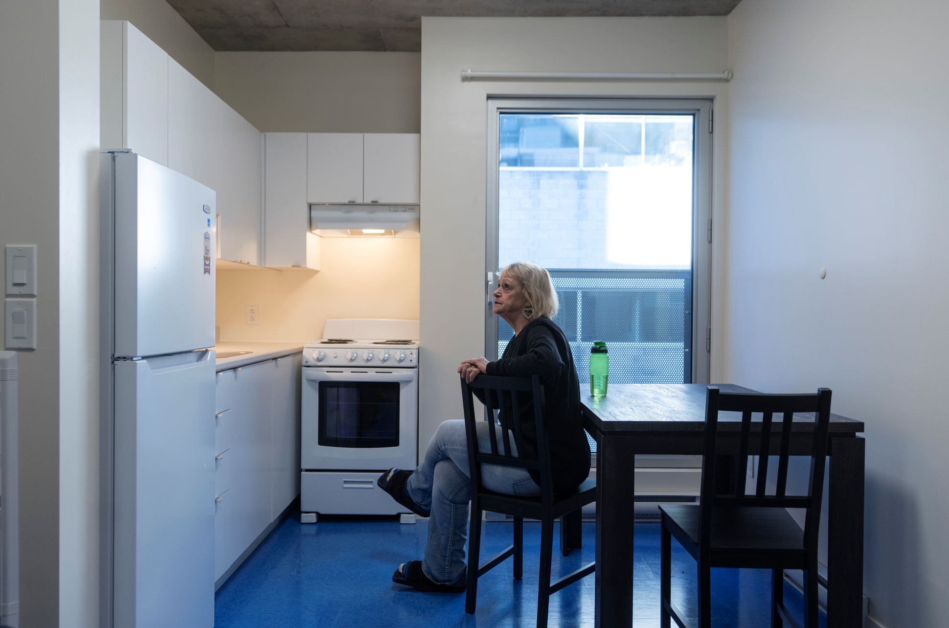 Une femme est assise à la table d’une petite cuisine dans un logement.