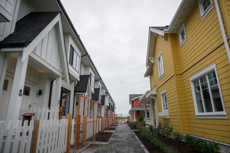 A row of white two-storey homes sits across from a couple standalone homes.