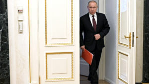 Russian President Vladimir Putin enters a room. He is dressed in a dark suit and tie, and has a red folder in one hand.