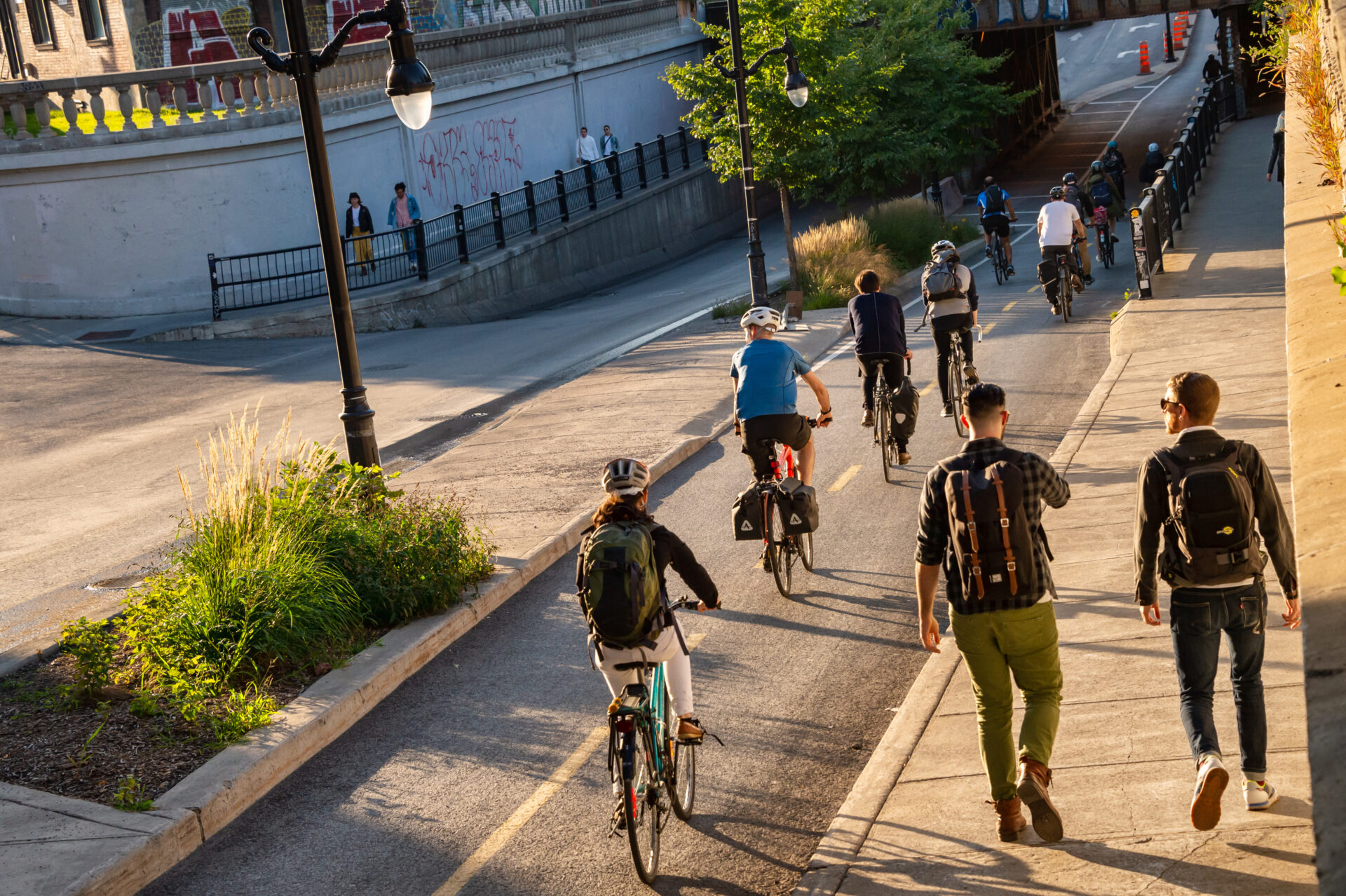 Eight cyclists use a two-way bike lane. A concrete median with curvy black light posts and planted decorative grass protects the cyclists from the lane for cars. There are no cars at the moment.