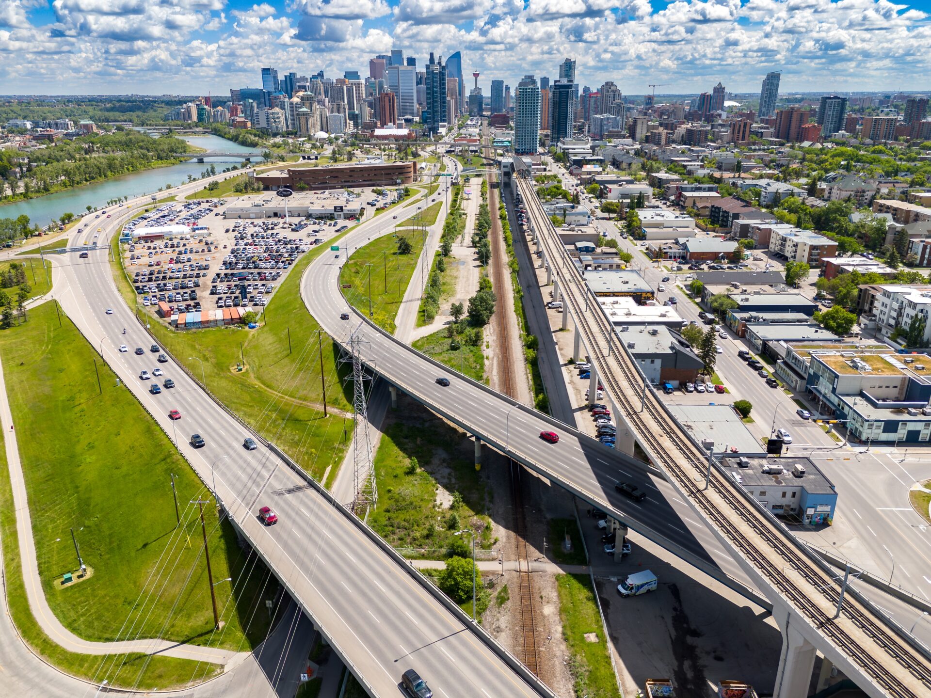 The city core is in the distance, with a cluster of glass towers. The highway and transit lines run through some green space and a part of town that has mixed-use low-rise buildings and small apartment buildings. The Bow river winds its way out of town.