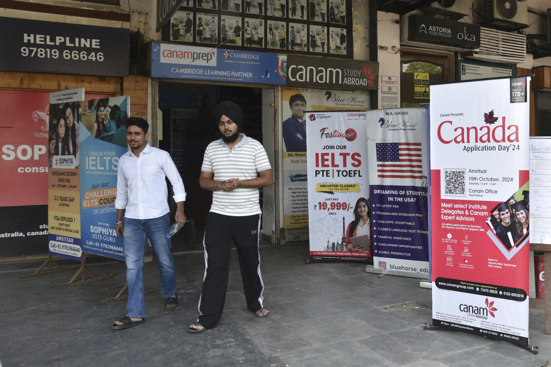 Two young men walk past five life-size posters positioned outside a building plastered with ads. Each poster advertises a study-abroad opportunity, including one for Canada. 