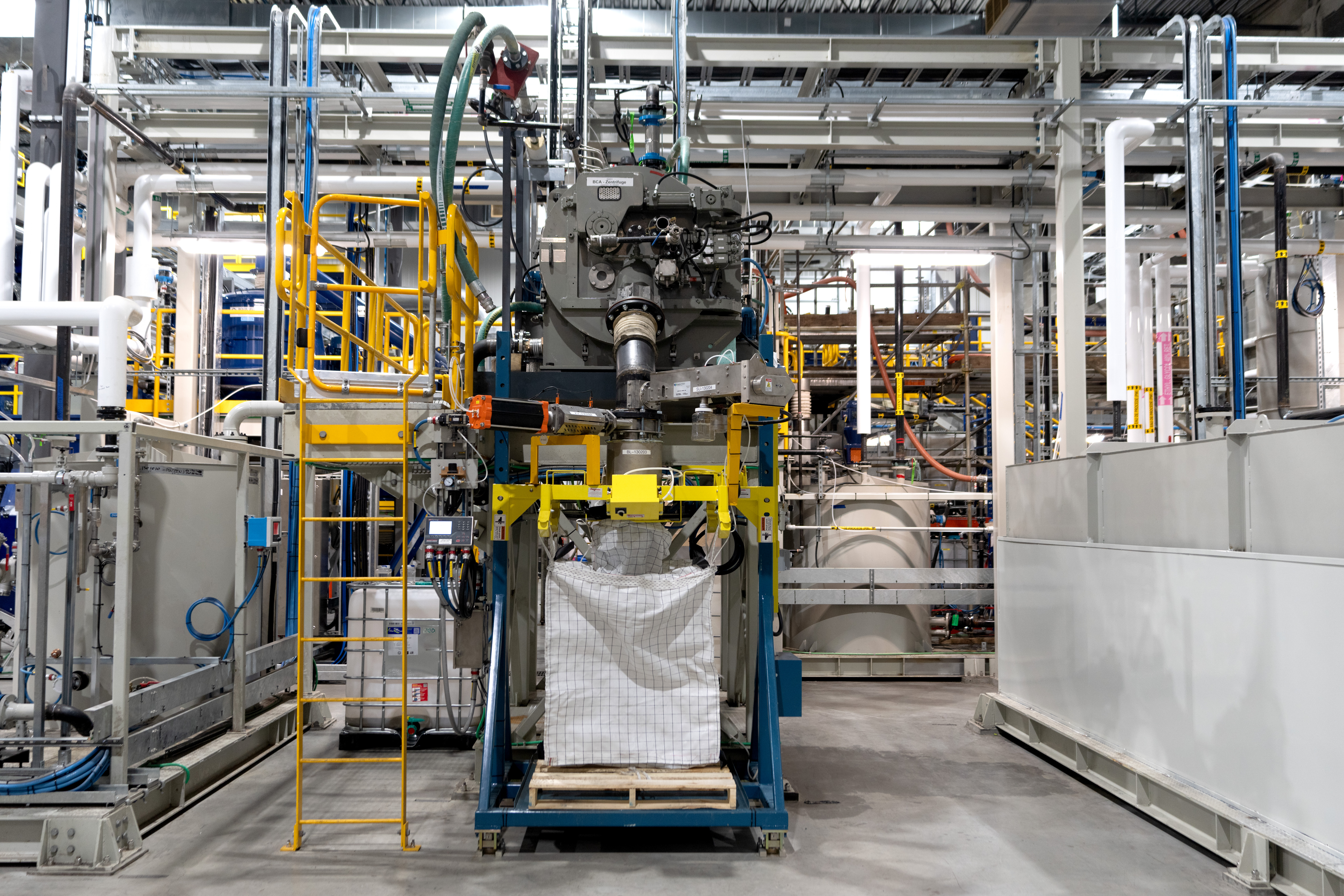 A floor of a factory filled with grey metal pipes, cords, and machinery.
